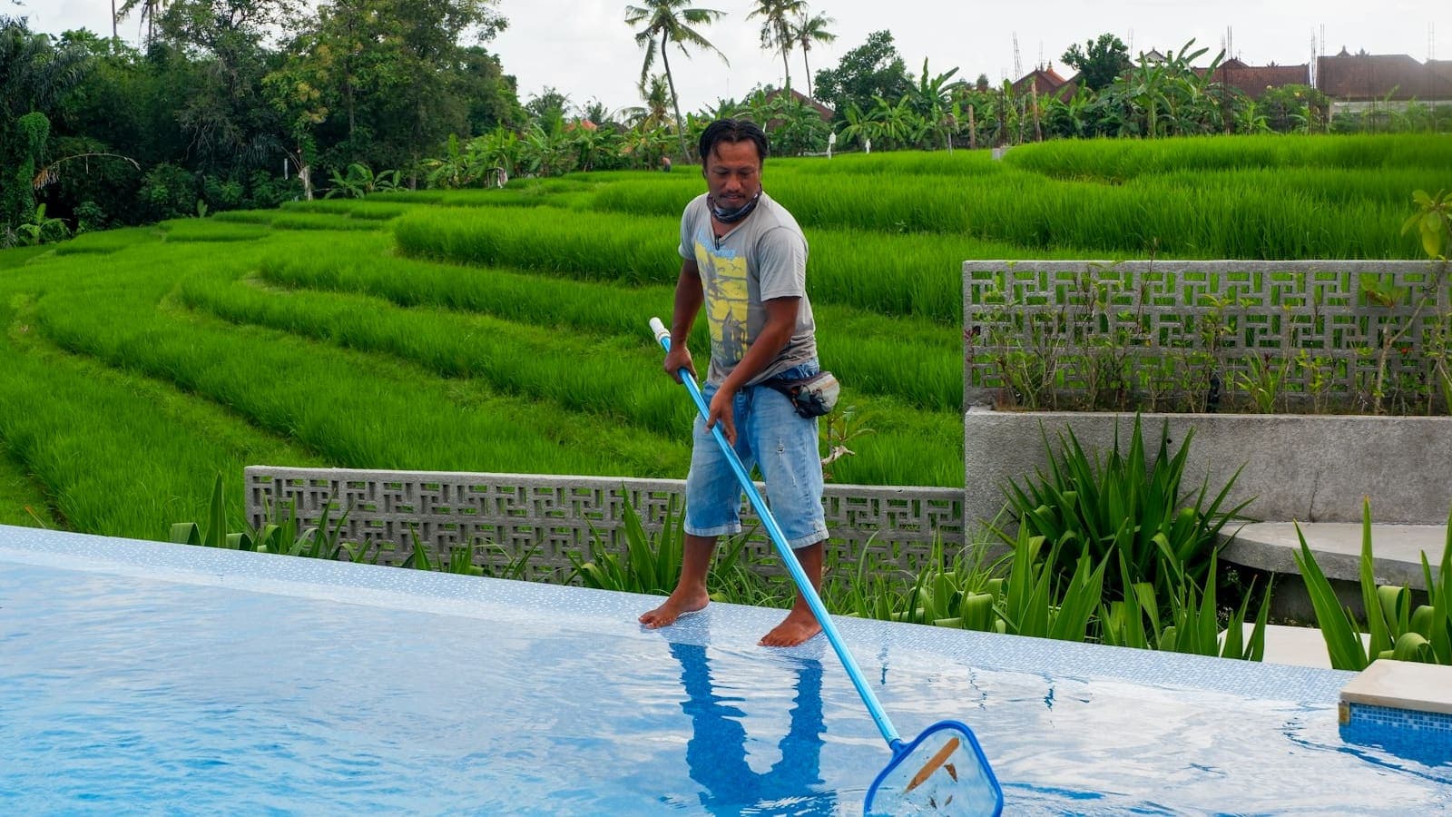 Pool service technician skimming a residential pool on a sunny day